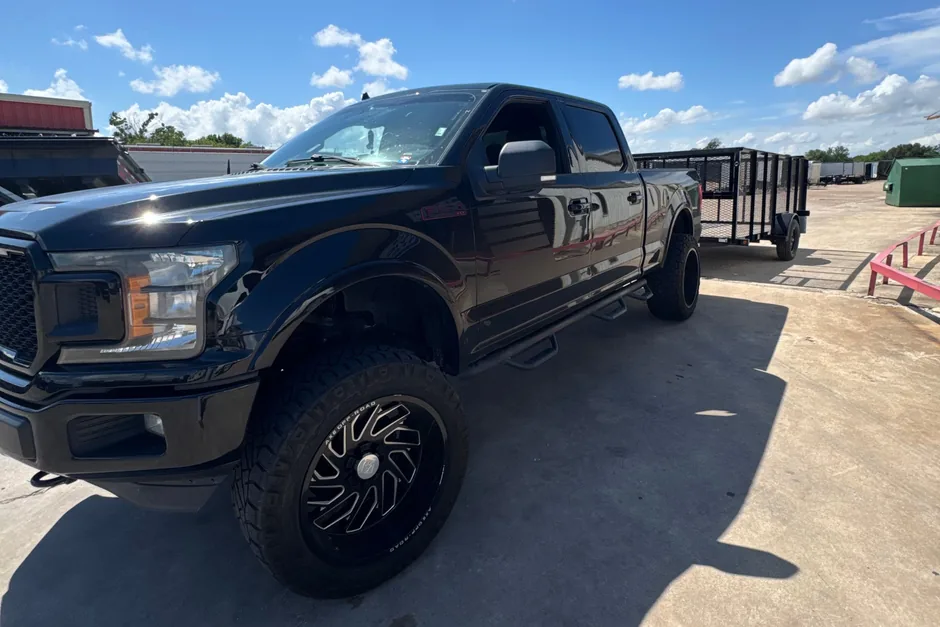 Black lifted Ford F-150 crew cab hitched to an open mesh-sided equipment trailer